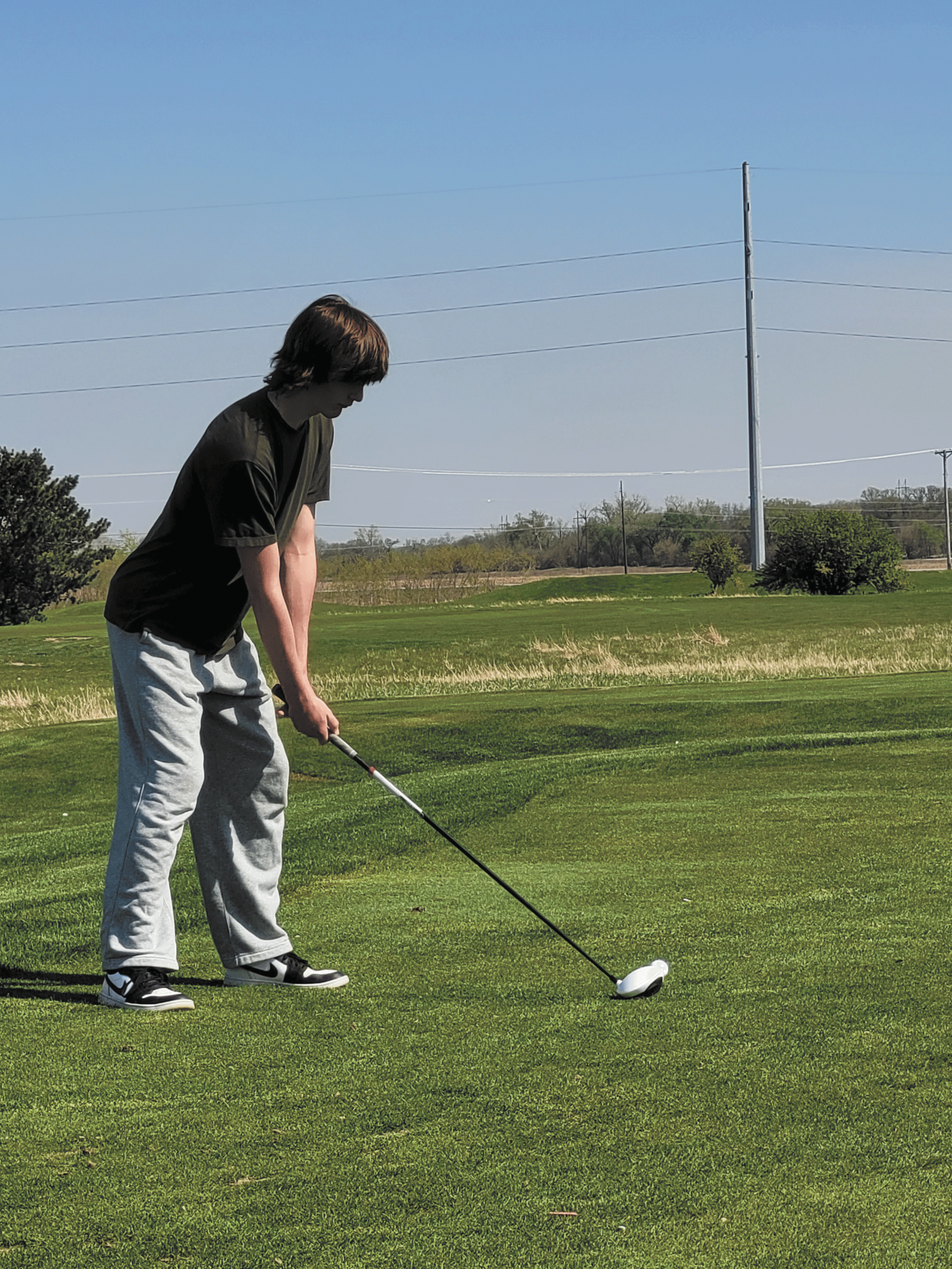 Concentrate. The sun shines over Eaagle Hills golf course on April 21, 2026, where junior Henry Perrin gets ready to make his first shot during a boy’s golf practice session. He took a moment to settle himself before carving out the shot so that his next ones would be just as focused, trying to keep his mentality neutral. “A lot of it is mental,” Perrin said. “If you score bad on a hole, and that’s all you think about, you’re not going to score well on any other hole.” 